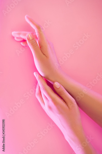 Woman s hands with perfect manicure in trendy neon light on pink background. Beauty concept.