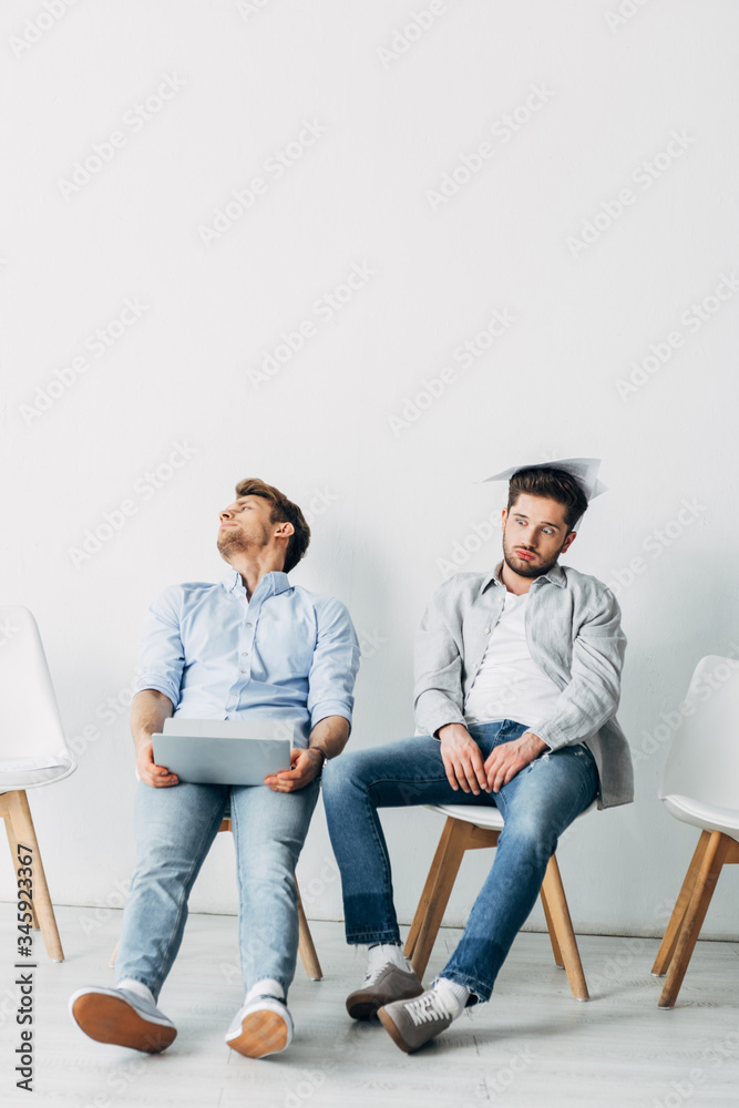 Tired applicants with resume and laptop sitting on chairs in office Tired applicants with resume and laptop sitting on chairs in office
