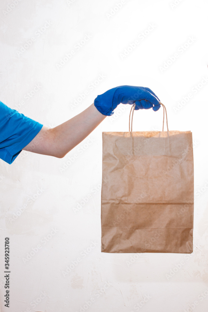 A hand in blue glove holds a craft paper package bag. Service coronavirus. Online shopping. mock up. Safe home delivery. A hand in blue glove holds a craft paper package bag. Service coronavirus. Online shopping. mock up. Safe home delivery.