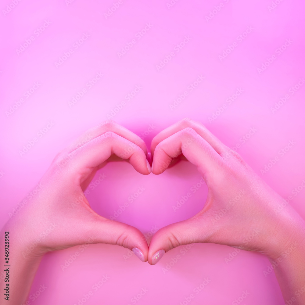 Obraz premium Young woman's hands made gesture of heart shape in trendy neon light on pink background. Love concept.