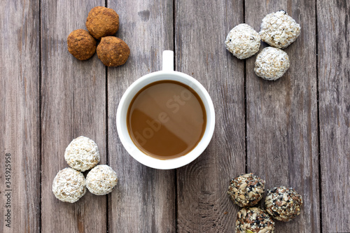 Healthy breakfast concept, four types of protein balls or energy bars on a wooden background in the center a white cup of coffee, horizontal orientation