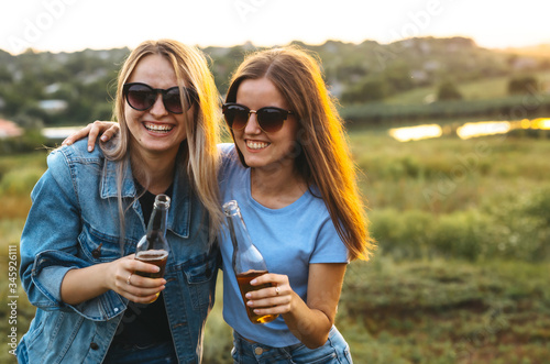 Two cheerful girls and young friends with sunglasses, drinking beer and enjoying the time spent together at sunset. Summer time.