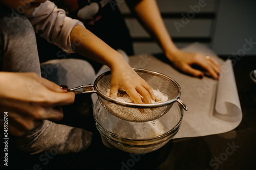 Little girl mixing flour with eggs, making dough. Mother and little daughter baking cookies at home.