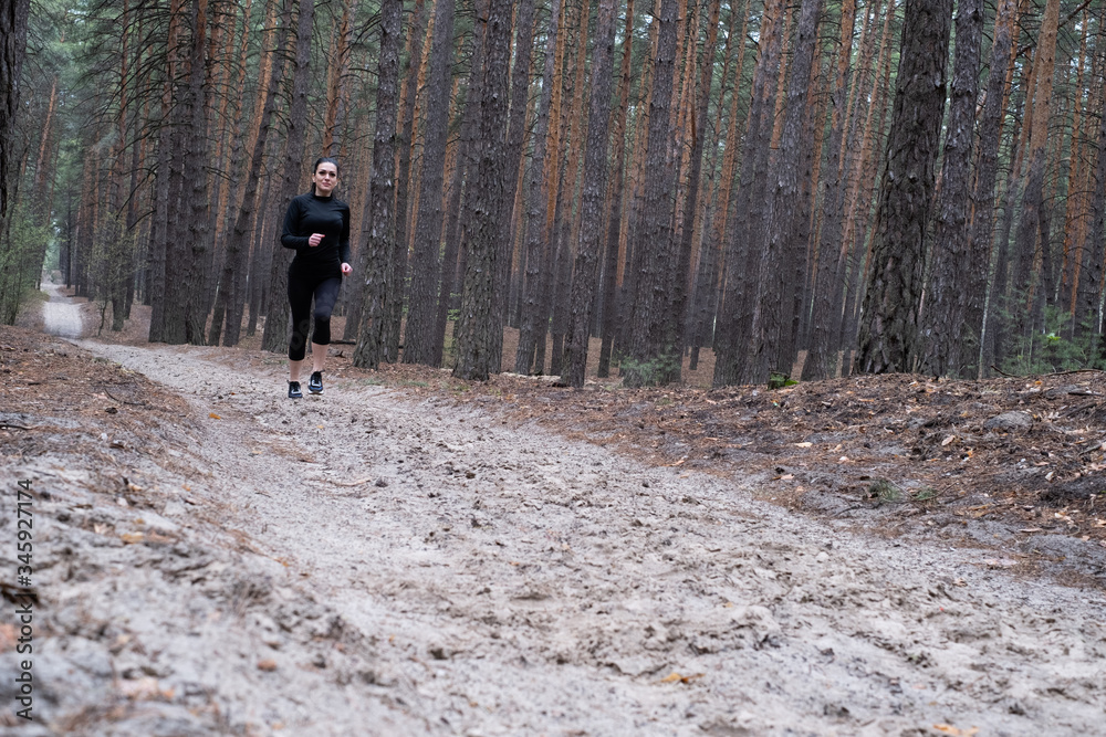girl with dark hair in black sportswear goes in for sports in the forest, jogging. Fitness during quarantine. Exercise during a pandemic. Jogging in the forest girl with dark hair in black sportswear goes in for sports in the forest, jogging. Fitness during quarantine. Exercise during a pandemic. Jogging in the forest