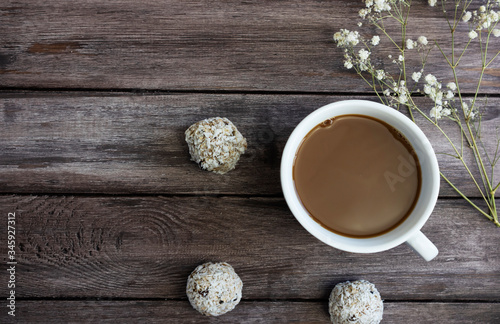 energy balls with a cup of coffee and white flowers on a wooden background, the concept of a healthy breakfast, copy space, healthy sweets, sweets from oatmeal, raisins in coconut flakes