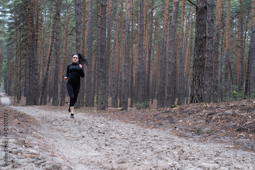 girl with dark hair in black sportswear goes in for sports in the forest, jogging. Fitness during quarantine. Exercise during a pandemic. Jogging in the forest