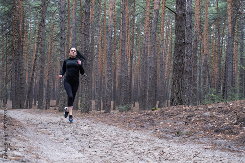 girl with dark hair in black sportswear goes in for sports in the forest, jogging. Fitness during quarantine. Exercise during a pandemic. Jogging in the forest