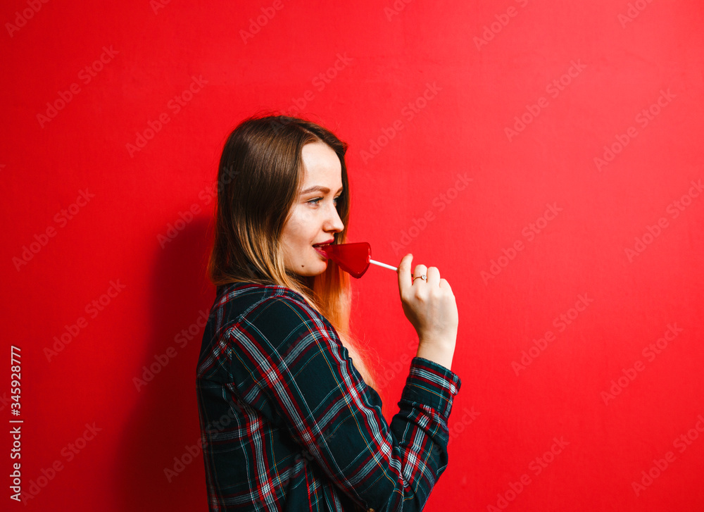 Beautiful brunette girl with a candy in her hand having fun on a red background. Beautiful brunette girl with a candy in her hand having fun on a red background.
