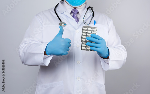 Fototapeta Naklejka Na Ścianę i Meble -  doctor therapist is dressed in a white uniform coat and blue sterile gloves is standing and holding a stack of pills in blister packs