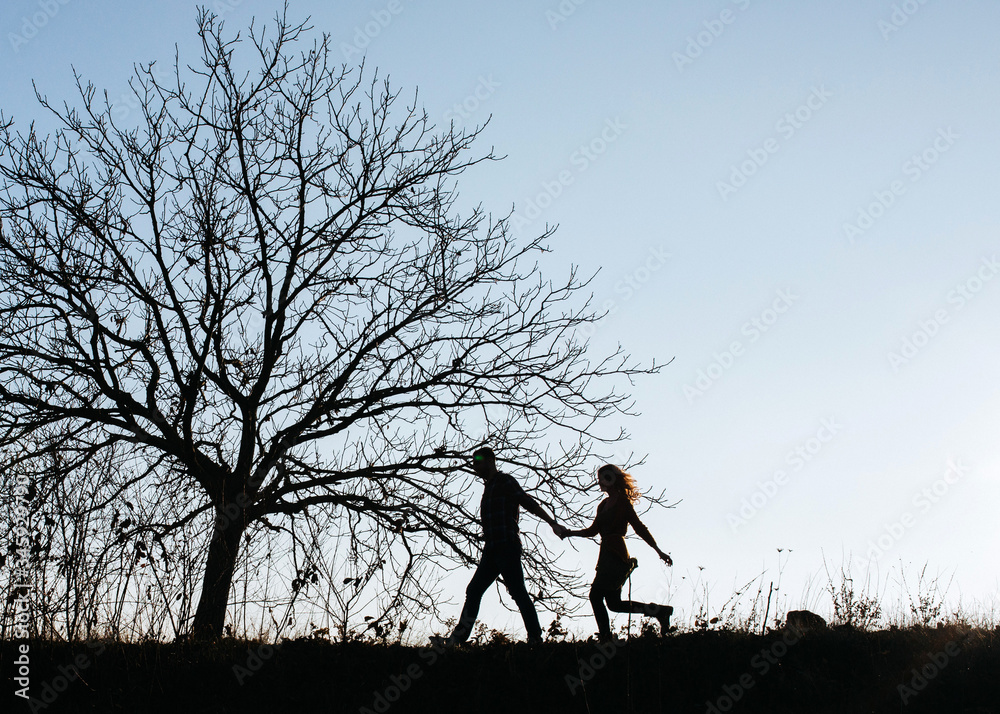 Silhouettes of a couple of man and woman outdoors, against sunset sky, walking between trees. Silhouettes of a couple of man and woman outdoors, against sunset sky, walking between trees.