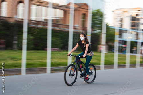 Chica joven de ojos claros, yendo en bicicleta durante coronavirus en una ciudad.