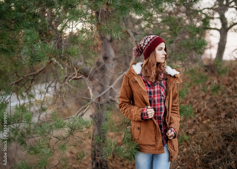 Portrait of a woman wearing warm clothes and a knitted cap,  standing outdoors in a forest.