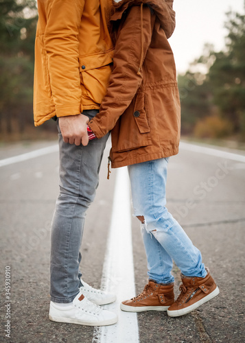 Young couple of man and woman, wearing warm clothes, holding hands and standing in the middle of an empty road.