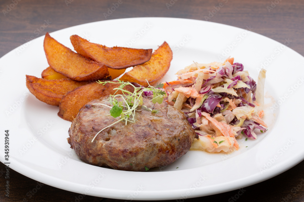 A burger with baked potatoes, cabbage and a salad in a ceramic plate on a wooden table A burger with baked potatoes, cabbage and a salad in a ceramic plate on a wooden table