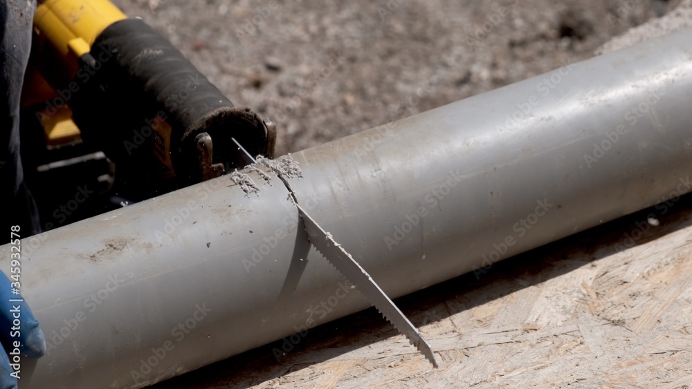 Plumber in rubber gloves, cuts the plastic sewer pipe, electric saber saw. Close-up. Plumber in rubber gloves, cuts the plastic sewer pipe, electric saber saw. Close-up.