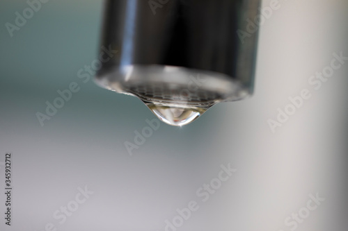 A closeup of a drop of water dripping from a tap with a blurry background