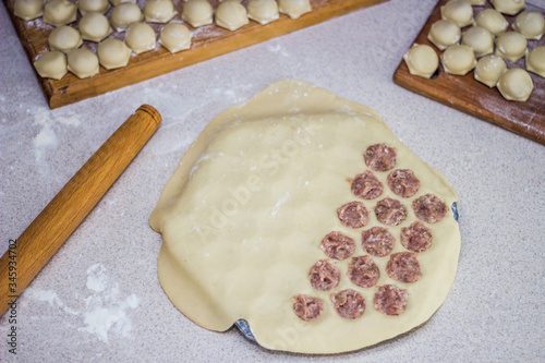 Traditional russian uncooked pelmeni on cutting board and ingredients for homemade pelmeni on white table. Process of making pelmeni, ravioli or dumplings with meat. Copy space. Side view.