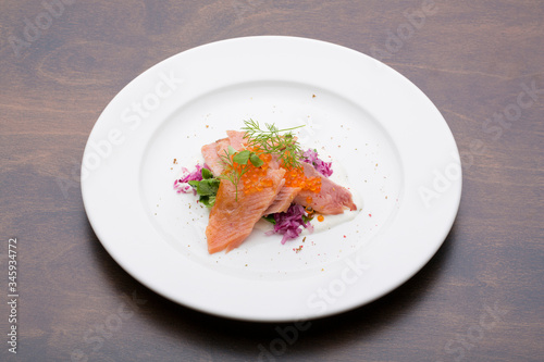Salmon with caviar on a white ceramic plate on a wooden table