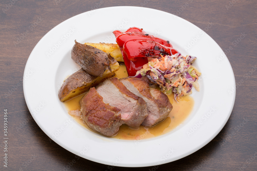 Sliced meat with paprika, potatoes and a salad on a white ceramic plate on a wooden table