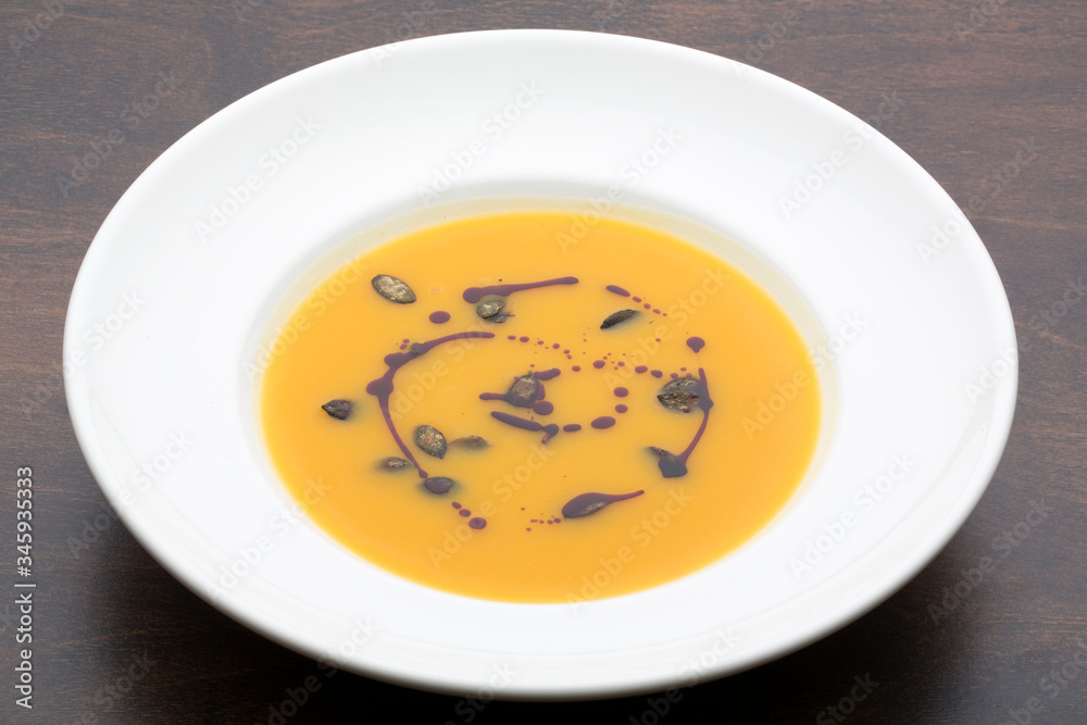 Yellow pumpkin soup in a white ceramic plate on a wooden table Yellow pumpkin soup in a white ceramic plate on a wooden table