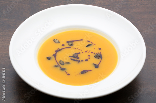 Yellow pumpkin soup in a white ceramic plate on a wooden table