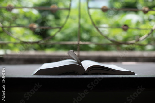 A book is kept open in front of a window with a page mark in a green background.