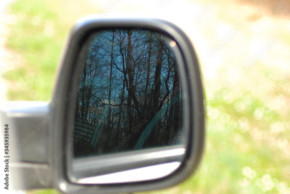  A spring forest and a blue sky are visible in a large car mirror.