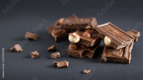 Milk chocolate pieces stack with hazelnut and crumbs on a black background. Closeup stacked bars of chocolate and nuts