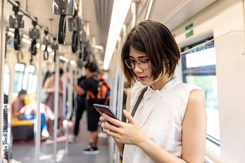 Asian young short hair woman wearing glasses using  and looking her smartphone in train