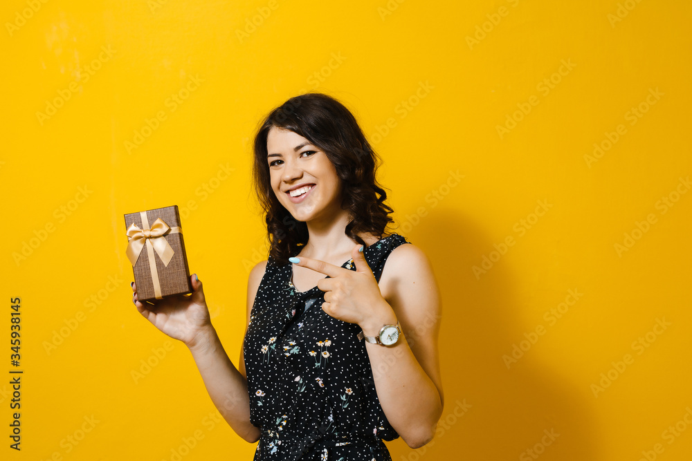 Portrait of a young beautiful asian girl holding a gift and happy over a yellow background Portrait of a young beautiful asian girl holding a gift and happy over a yellow background