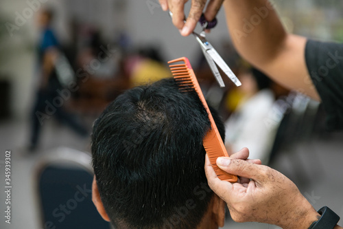 Hand of barber trimming hair of man with scissors and comb at barber shop