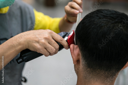 Hand of barber trimming hair of man with hair clipper and comb at barber shop