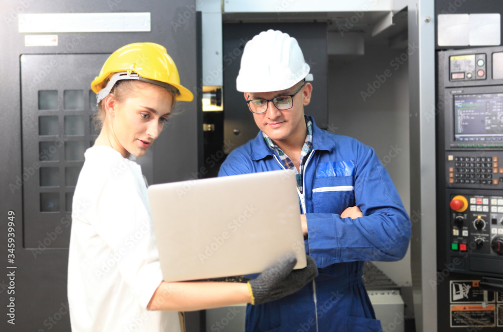 Male and Female Industrial Engineers in Hard Hats Discuss New Project while Using Laptop. They Work in a Heavy Industry Manufacturing Factory. Male and Female Industrial Engineers in Hard Hats Discuss New Project while Using Laptop. They Work in a Heavy Industry Manufacturing Factory.