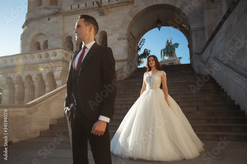 Obraz na płótnie Bride and groom hugging in the old town street. Wedding couple walking on the Fisherman's Bastion, Budapest, Hungary. Happy romantic young couple celebrating their marriage. Wedding and love concept. w salonie
