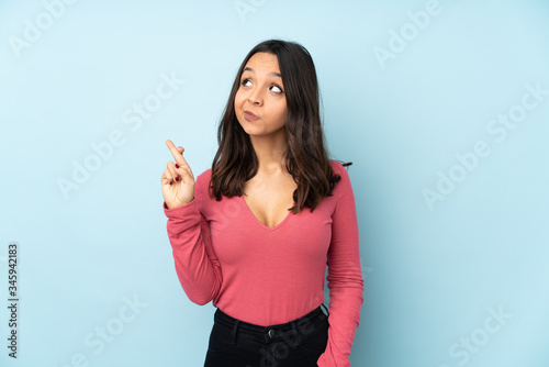 Young mixed race woman isolated on blue background with fingers crossing and wishing the best