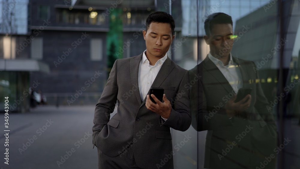 Front view of a young asian businessman, leading correspondence on the phone. Financial business area.