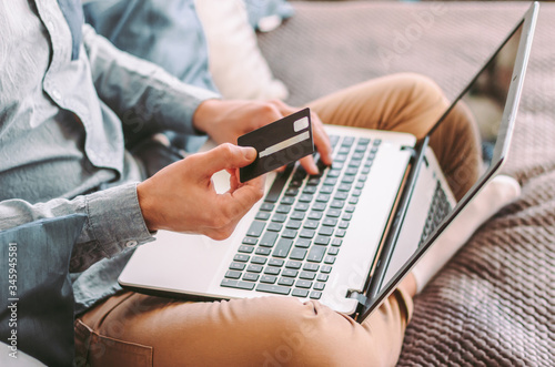 Closeup young hipster male shopper hold credit card and type on laptop keyboard, shopping online, working at home. Stylish man freelancer using computer for internet purchase, payment. E-commerce