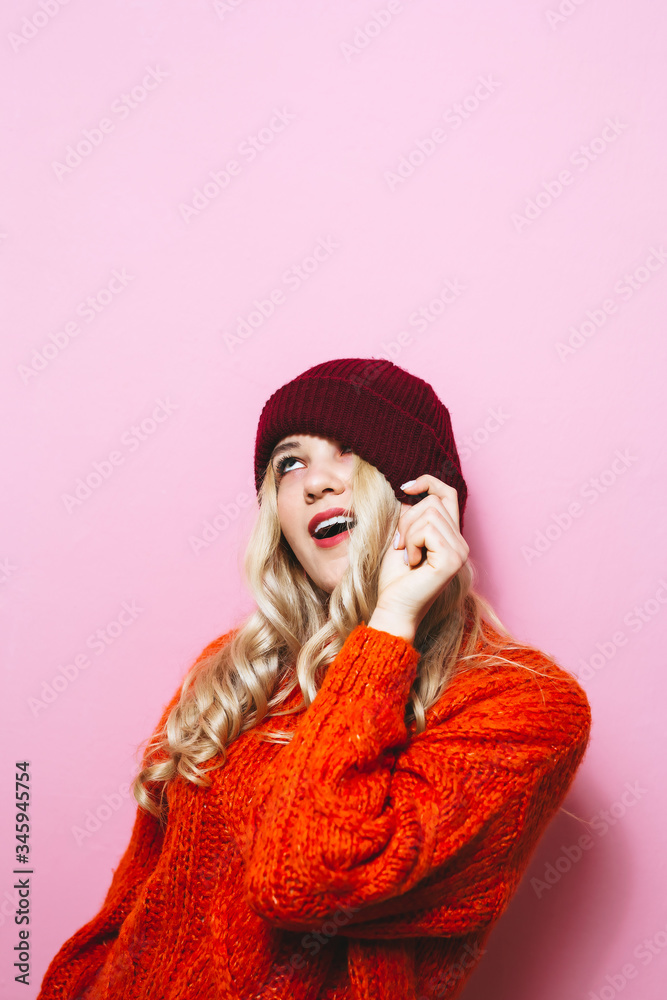Portrait of smiling blonde girl in winter hat over pink background.
Portrait of smiling blonde girl in winter hat over pink background.