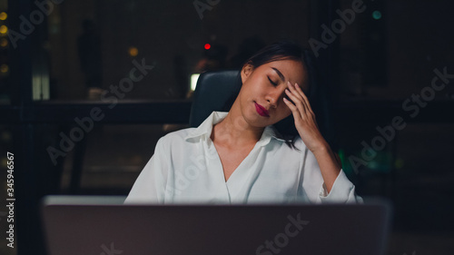 Millennial young Chinese businesswoman working late night stress out with project research problem on laptop in meeting room at small modern office. Asia people occupational burnout syndrome concept.