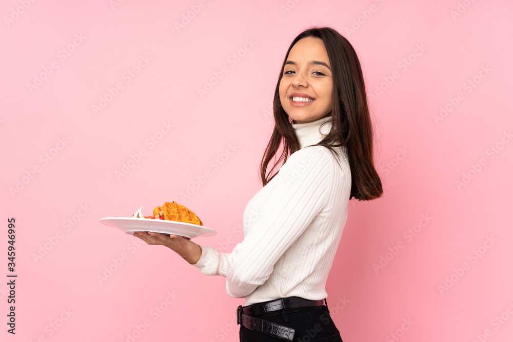Young brunette woman holding waffles over isolated pink background with arms crossed and looking forward Young brunette woman holding waffles over isolated pink background with arms crossed and looking forward