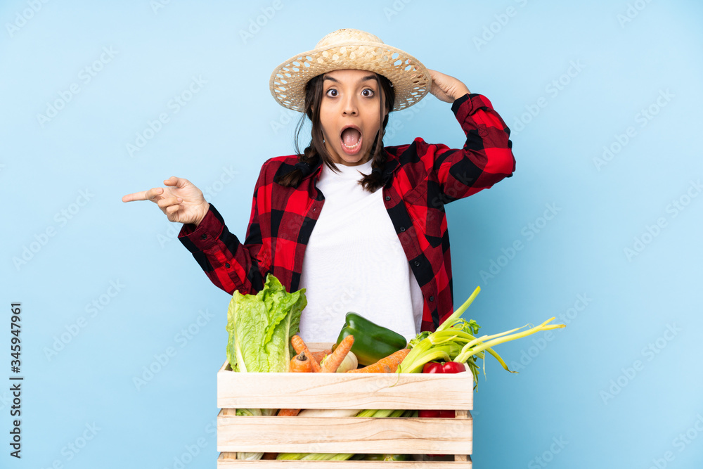 Young farmer Woman holding fresh vegetables in a wooden basket surprised and pointing finger to the side