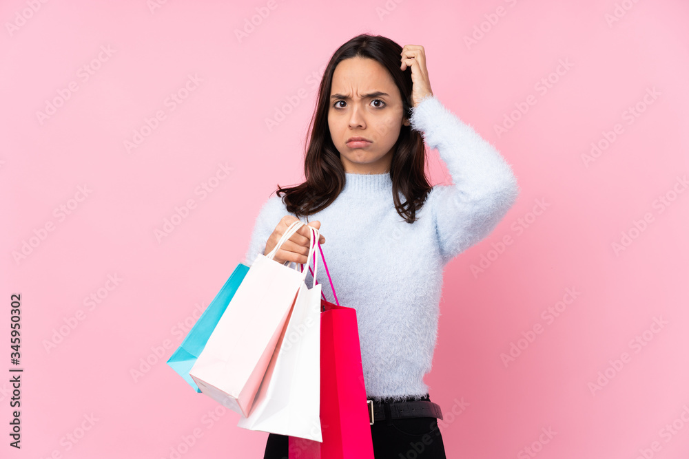 Young woman with shopping bag over isolated pink background having doubts
