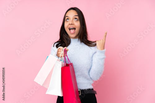 Young woman with shopping bag over isolated pink background pointing up and surprised
