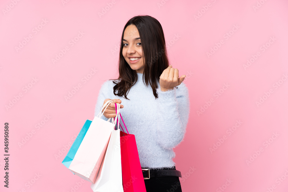 Young woman with shopping bag over isolated pink background inviting to come with hand. Happy that you came