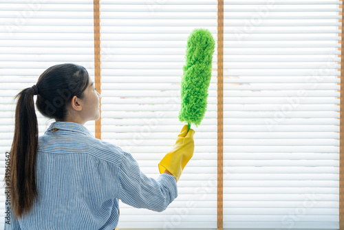Young female spring cleaning house interior holding a duster for wiping dust dusting furniture at home. photo