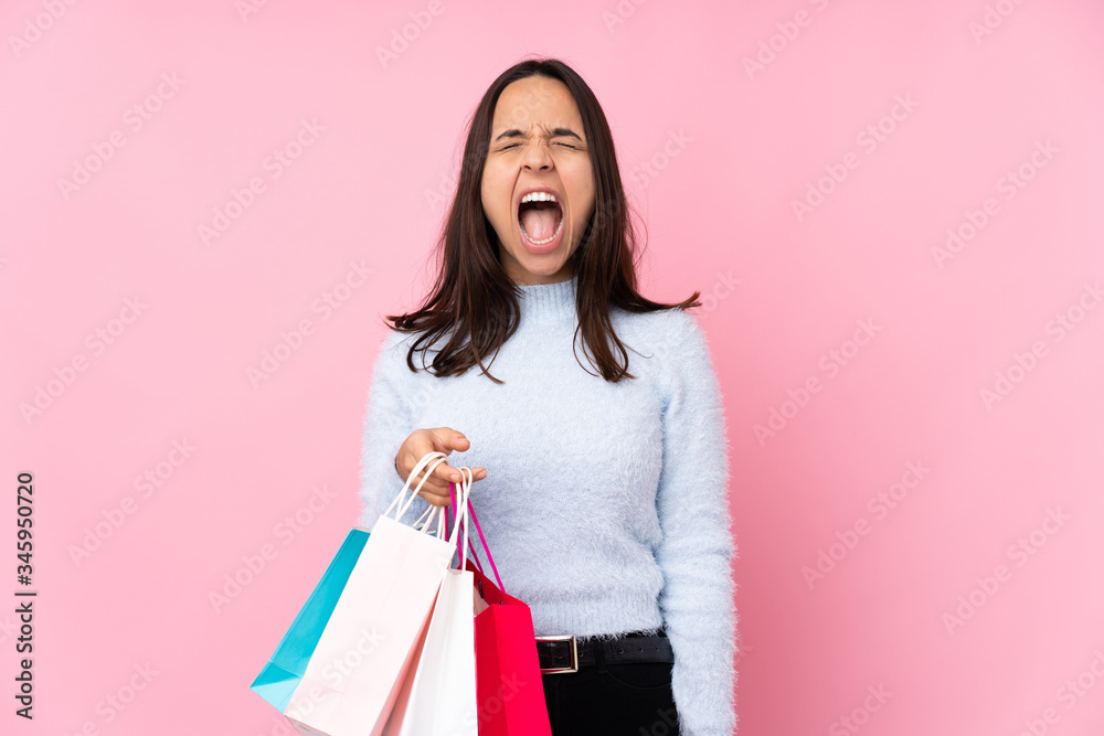 Young woman with shopping bag over isolated pink background shouting to the front with mouth wide open