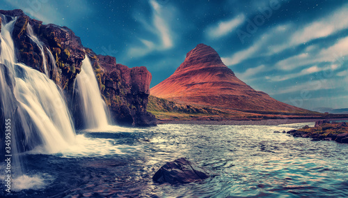 Wonderful Evening View of Kirkjufell waterfall with stars sky over the Kirkjufell mount. Scenic image of Iceland. long exposure shot. scenery of tipical Icelandic nature with Northern Lights. postcard