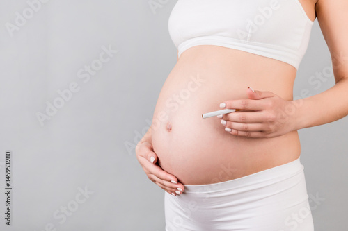 Close up of pregnant woman in white underwear with a cigarette against her belly at gray background. Dangerous risk for unborn baby © sosiukin