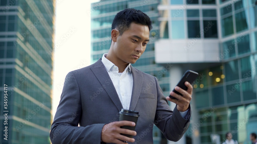 Portrait shot of a young asian businessman, leading correspondence on the phone with coffee in his hands. Financial business area. Portrait shot of a young asian businessman, leading correspondence on the phone with coffee in his hands. Financial business area.