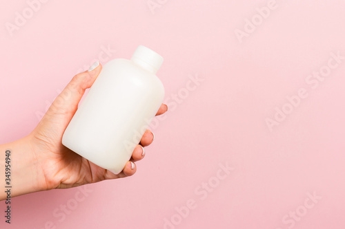 Close up of cosmetics bottle in female hand at pink background with copy space